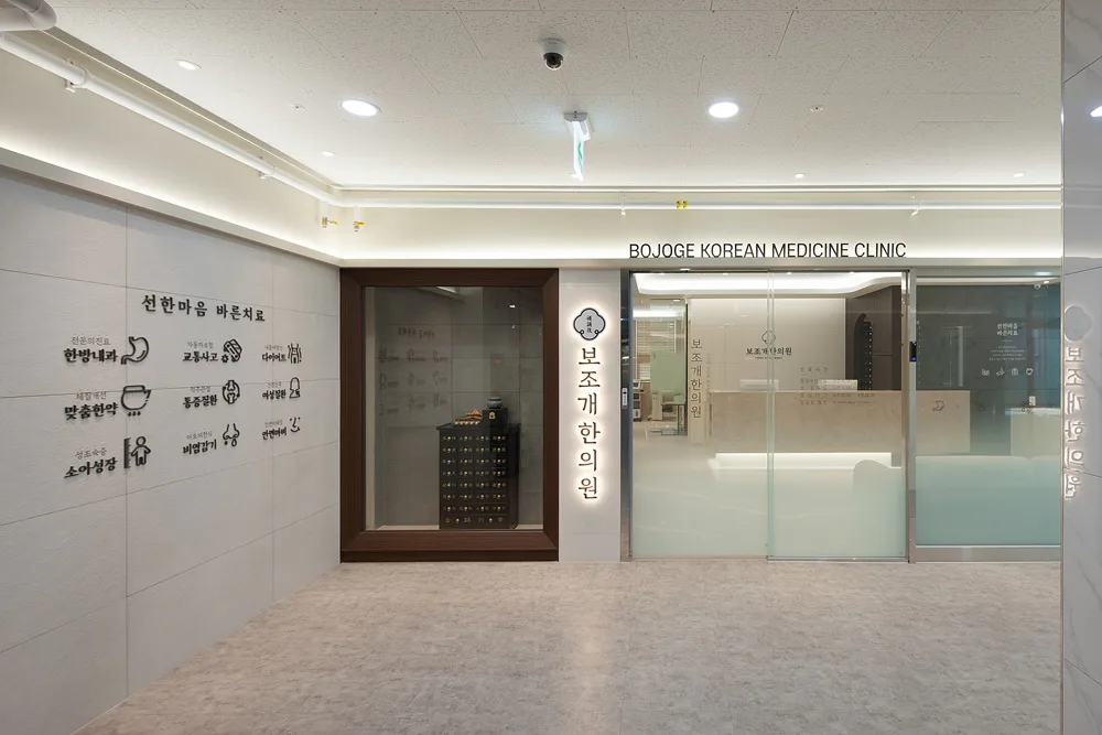 보조개한의원 입구 복도. 영문 사인 BOJOGE KOREAN MEDICINE CLINIC 과 진료과목 아이콘 벽
